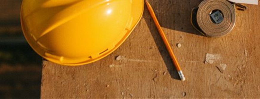 Casco giallo, matita e metro a nastro sul piano di legno di un tavolo da cantiere